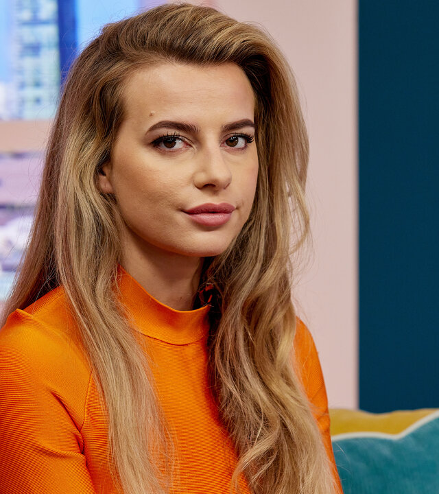 "Kidnapped: The Chloe Ayling Story – Die Entführung": Chloe Ayling (Nadia Parkes) sitzt in einem bunt dekorierten TV-Studio auf einem Sofa.