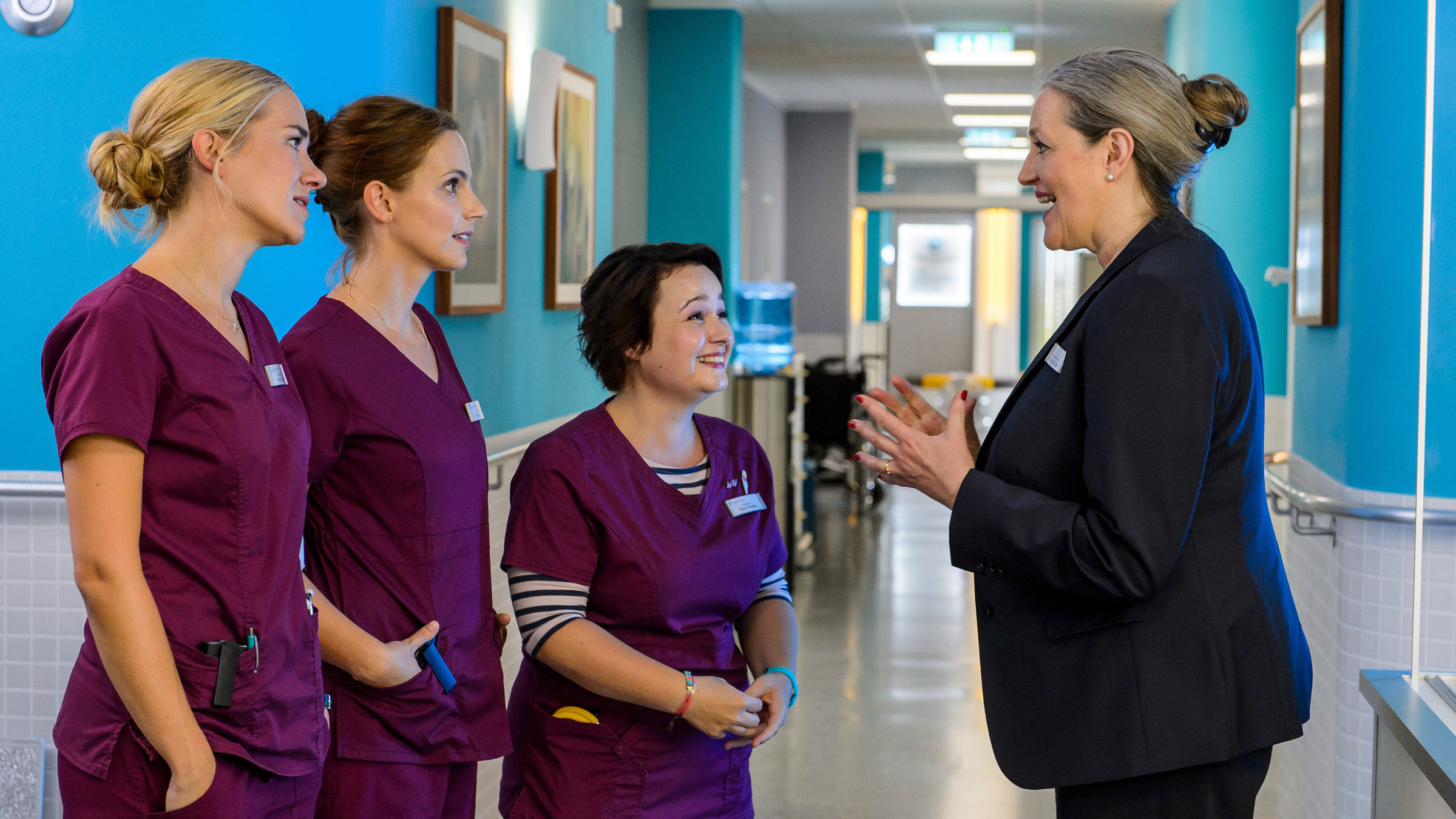 "Bettys Diagnose - Um Haaresbreite": Betty Weiss (Annina Hellenthal), Hanna Winter (Marie Zielcke) und Talula Pfeifer (Carolin Walter) nehmen auf dem Krankenhausflur freudig eine Neuigkeit von Mechthild Puhl (Sybille J. Schedwill) entgegen.