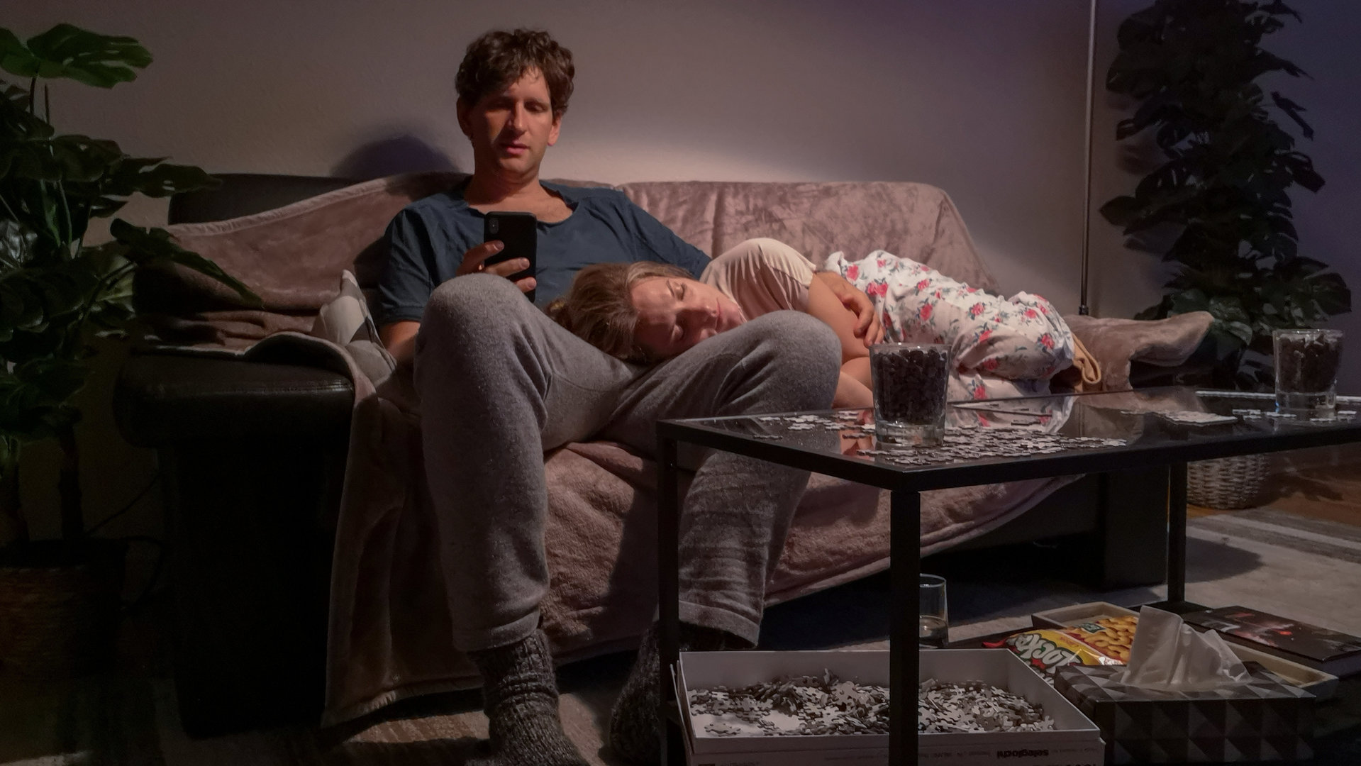 "Liebe. Jetzt! - Der Kuss":  Heiner (Sebastian Schwarz) sitzt mit seinem Handy auf dem Sofa. Seine Frau Meike (Marie Burchard) liegt schlafend auf seinem Schoß.