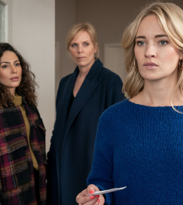 "SOKO Leipzig - Unter die Haut": Kim Nowak (Amy Mußul) und Ina Zimmermann (Melanie Marschke) stehen hinter Sandy Lanz (Valerie Huber) in Sandys Wohnung. Sandy hat den Kommissarinnen den Rücken zugewandt. Sie hält einen Zettel in der Hand und schaut gedankenverloren zur Seite.