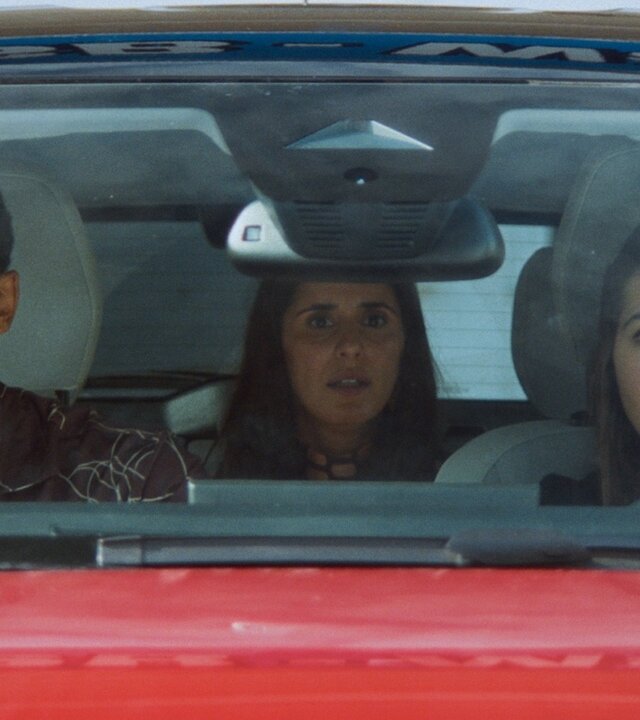 "Doppelhaushälfte – Fahrerlaubnis": Zoe Sawadi (Helena Yousefi) sitzt am Steuer eines Autos, neben ihr auf dem Beifahrersitz sitzt Theo Kröger (Benito Bause), hinter den beiden auf der Rückbank sitzt Mari Sawadi (Maryam Zaree). Alle blicken erschrocken nach vorne.