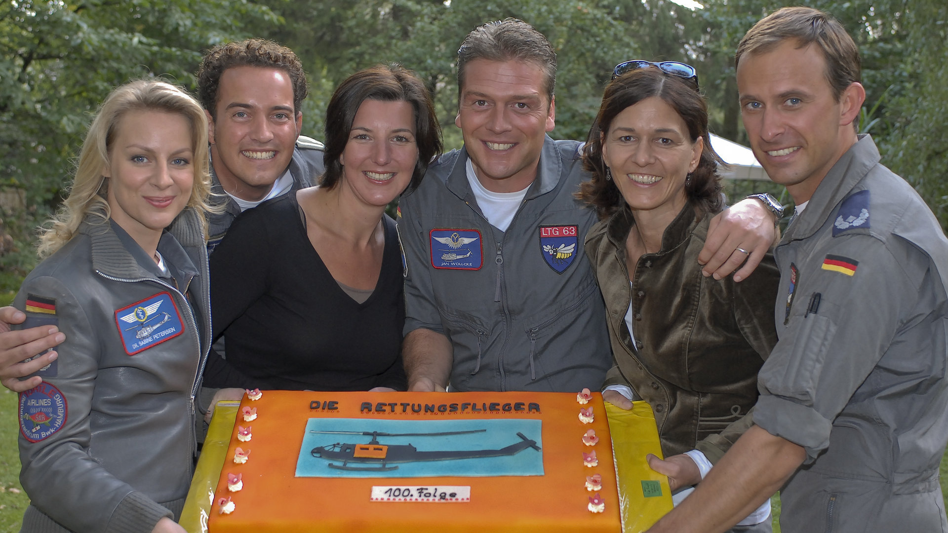 "Die Rettungsflieger": Das Team der Rettungsflieger hält gemeinsam eine Torte - darauf ist das Bild eines Hubschraubers zu sehen, darunter der Schriftzug "100. Folge".