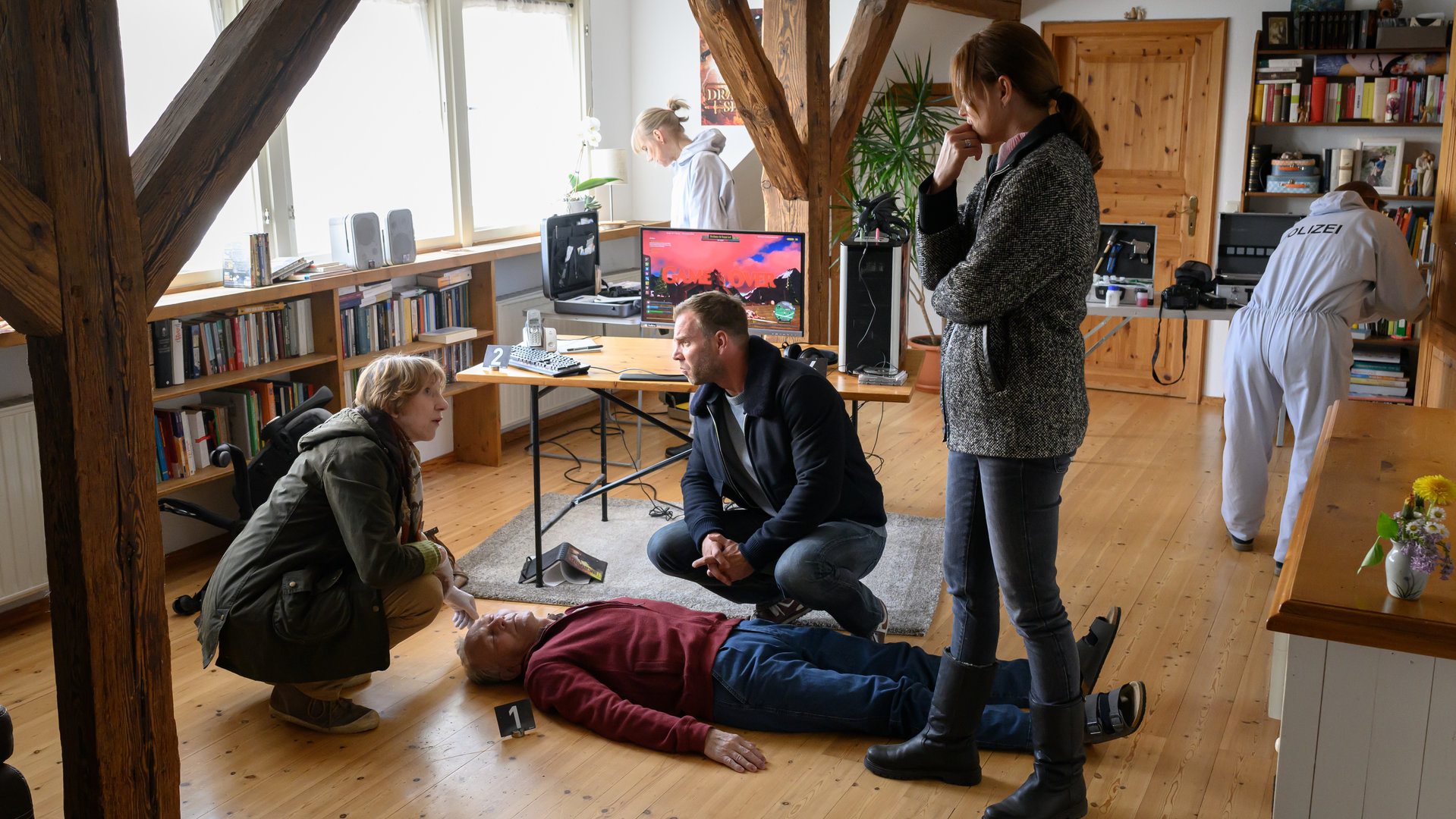 "SOKO Wismar - Game Over": Dr. Helene Sturbeck (Katharina Blaschke) kniet neben der leiche und klärt die Kommissarin Karoline Joost (Nike Fuhrmann) und Kommissar Lars Pöhlmann (Dominic Boeer) über die Todesursache von Reinhold Graf (Günter Petri) auf.