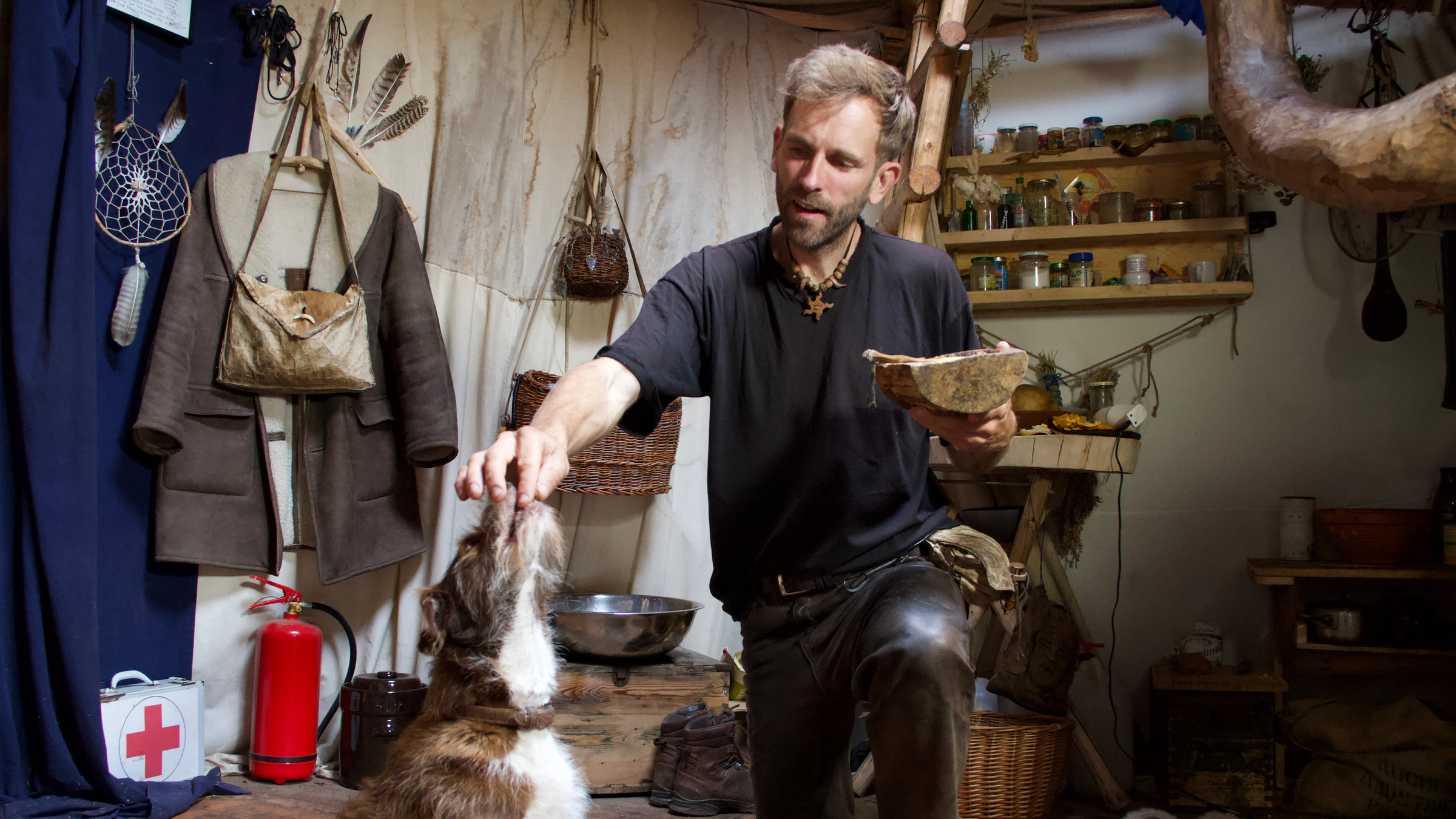 "37°: Schluss mit Überfluss - Von Minimalisten und Konsumverweigerern": Marc füttert seinen Hund im Inneren einer rustikalen Hütte.