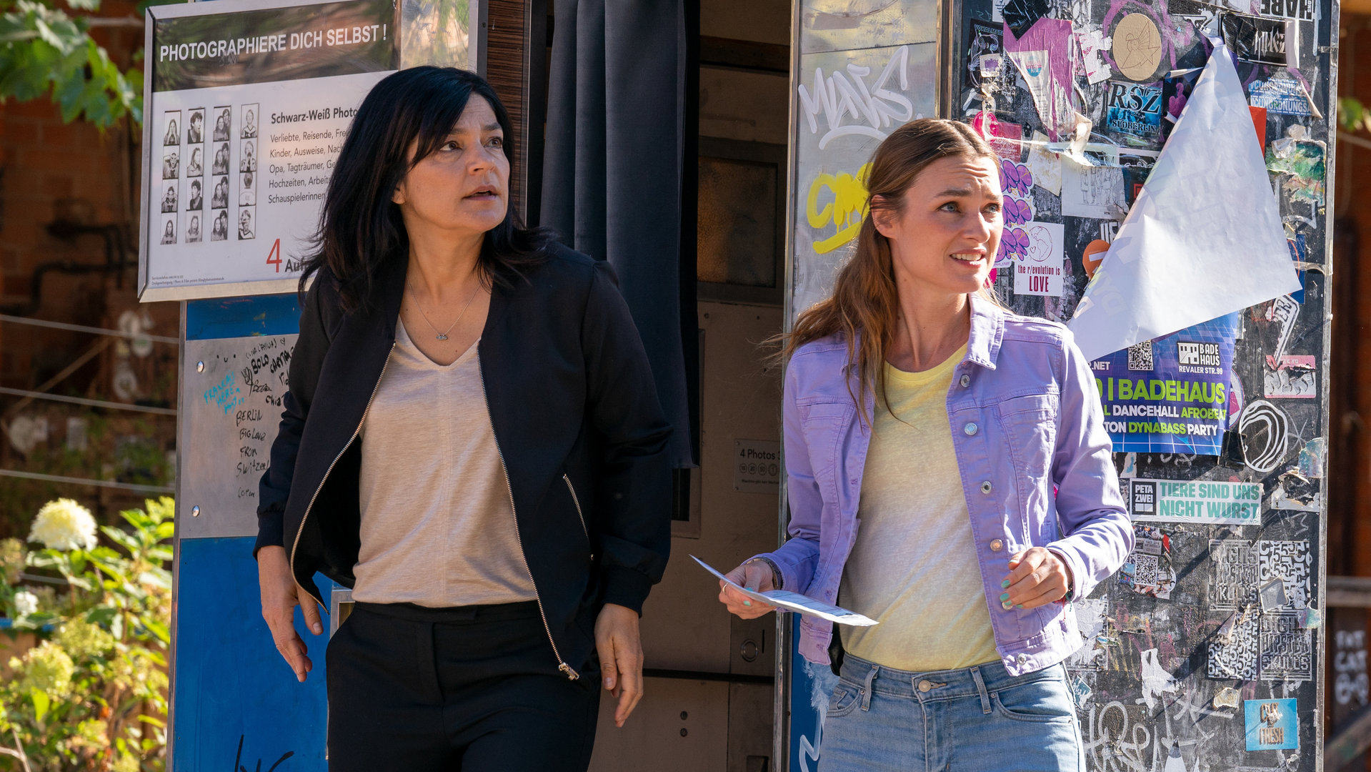"Letzte Spur Berlin - Padam!": Mina Amiri (Jasmin Tabatabai) und Lucy Elbe (Josephin Busch) stehen auf der Straße vor einem Fotoautomaten. Beide schauen verblüfft nach rechts.