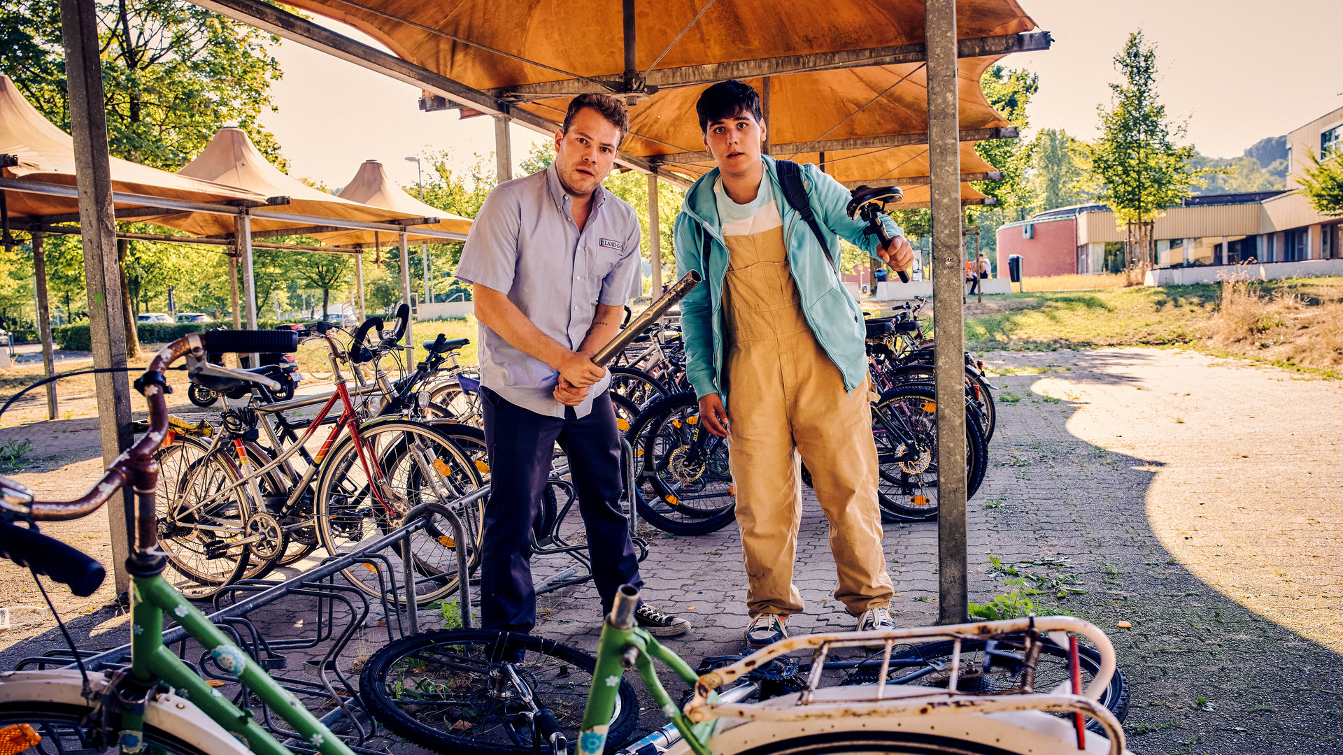 "Like a Loser - Aus Spaß wurde Ernst": Julian (Ben Münchow) und Ernst (Diyar Ilhan) stehen an einem Abstellplatz für Fahrräder und blicken erschrocken auf. Vor ihnen liegt ein umgeworfenes und beschädigtes Fahrrad. Julian umklammert mit beiden Händen ein Stahlrohr. Ernst hält in der linken Hand einen Fahrradsitz.