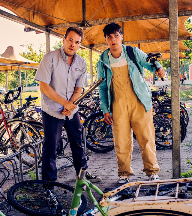 "Like a Loser - Aus Spaß wurde Ernst": Julian (Ben Münchow) und Ernst (Diyar Ilhan) stehen an einem Abstellplatz für Fahrräder und blicken erschrocken auf. Vor ihnen liegt ein umgeworfenes und beschädigtes Fahrrad. Julian umklammert mit beiden Händen ein Stahlrohr. Ernst hält in der linken Hand einen Fahrradsitz.