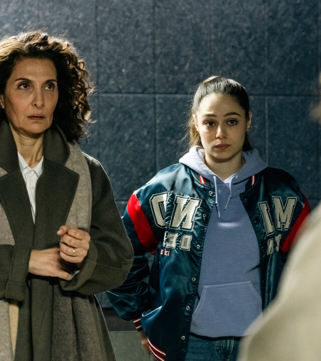 "SOKO Köln - Die Frau auf dem roten Fahrrad": Yasmin Barani (Proschat Madani) steht neben Amira Mahdi (Aylin Ravanyar) vor einer dunkelgrauen Wand mit Fliesenmuster. Sie blickt angespannt nach oben. Amira hat die Arme in die Hüften gestemmt und sieht ernst zu Lilly Funke (Tatjana Kästel), die ihr gegenüber steht, mit dem Rücken zur Kamera.