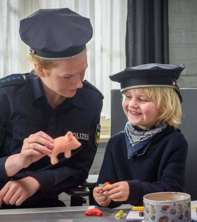 "SOKO Wismar - Wie das Leben spielt": Paula Moorkamp (Stella Hinrichs) sitzt neben Tim Kern (Yvon Sable Moltzen) an ihrem Schreibtisch. Paula spielt mit einem Plastikschwein und Tim ist sichtlich erfreut. Im Vordergrund befinden sich ein Bildschirm, eine Tasse, sowie mehrere Dokumente.