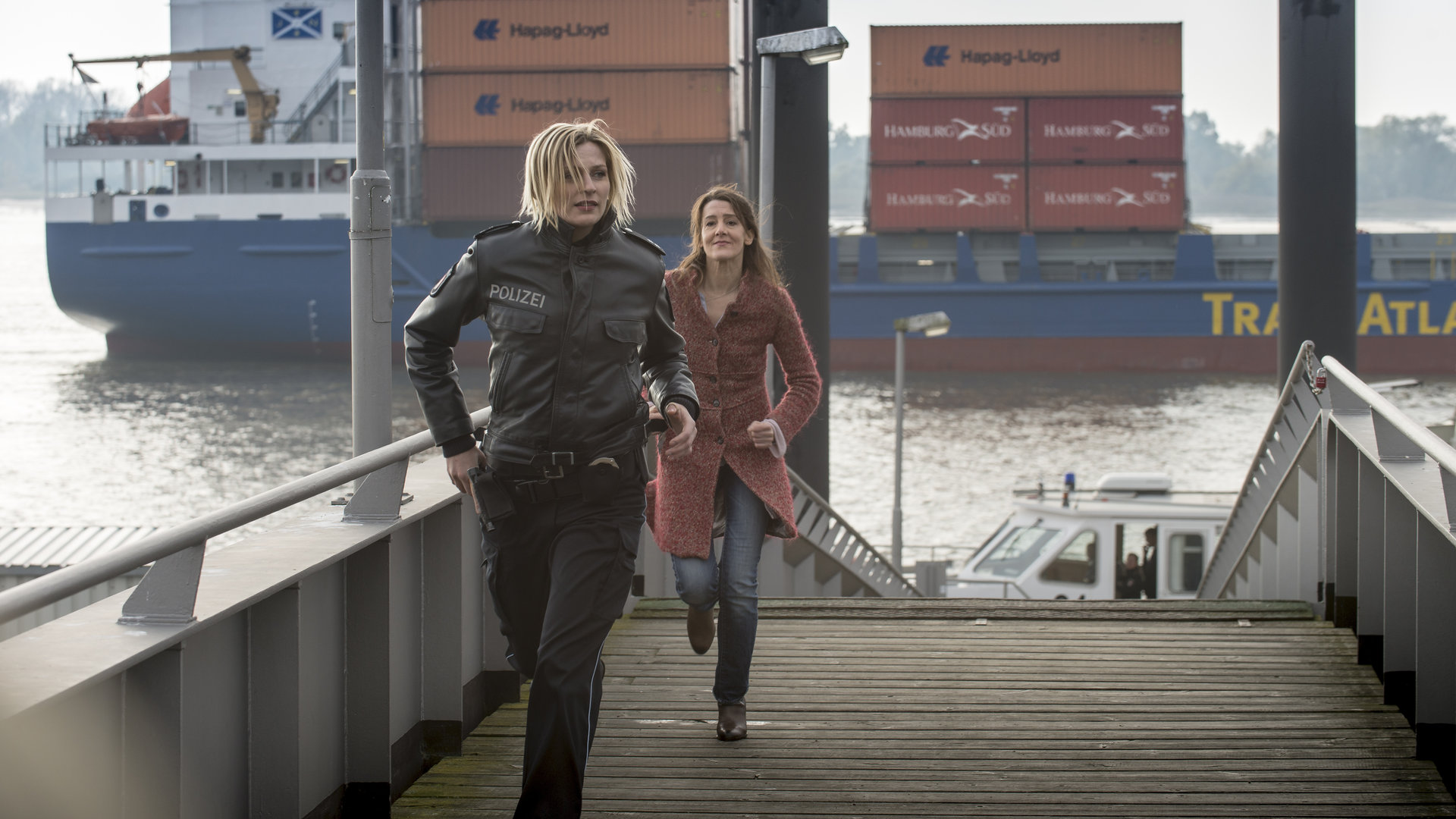 "Notruf Hafenkante - Gelegenheit macht Diebe": Melanie (Sanna Englund) und die Mutter des verschwundenen Kindes (Ursula Doll) rennen an einem Pier entlang. Im Hintergrund fährt ein Containerschiff.
