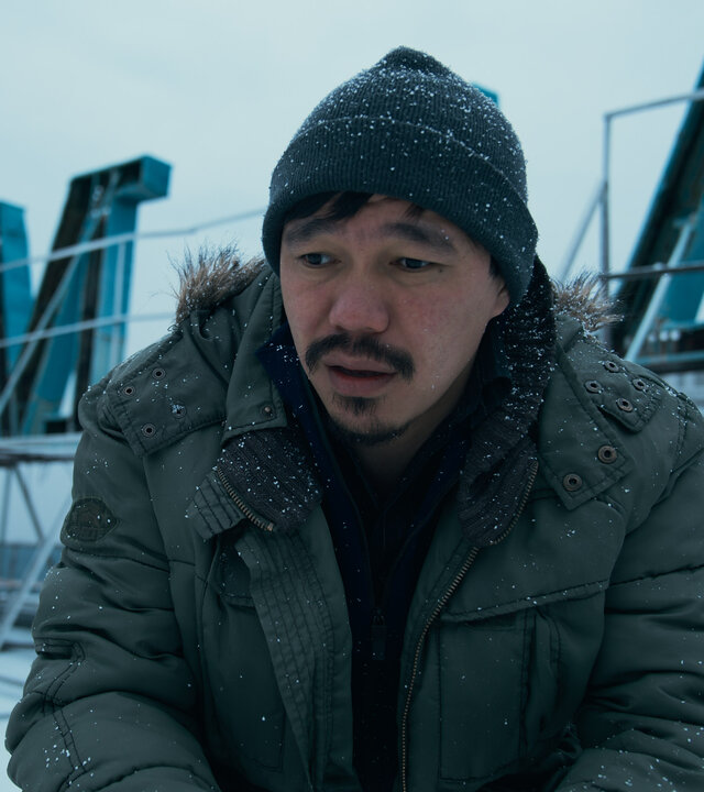 "Infiniti - Turm zu Babel": Isaak (Daniyar Alshinov) kniet auf einem verschneitem Dach und schaut konzentriert in die Ferne. Im Hintergrund ist der kyrillische Schriftzug des Gebäudes zu erkennen.