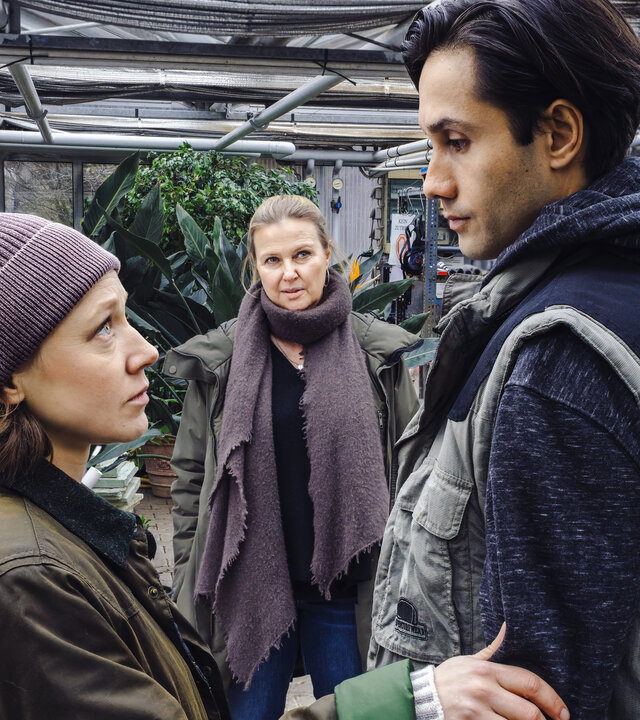 "Die Chefin - Gefallener Engel": In einem Gewächshaus steht Vera Lanz (Katharina Böhm) und schaut zu Alexandra Pedri (Katharina Leonore Goebel, l.) und Gonzalo Pedri (Conrad Ahrens, r.). Die beiden stehen sich gegenüber und schauen sich an, Alexandra hält Gonzalo am Arm.