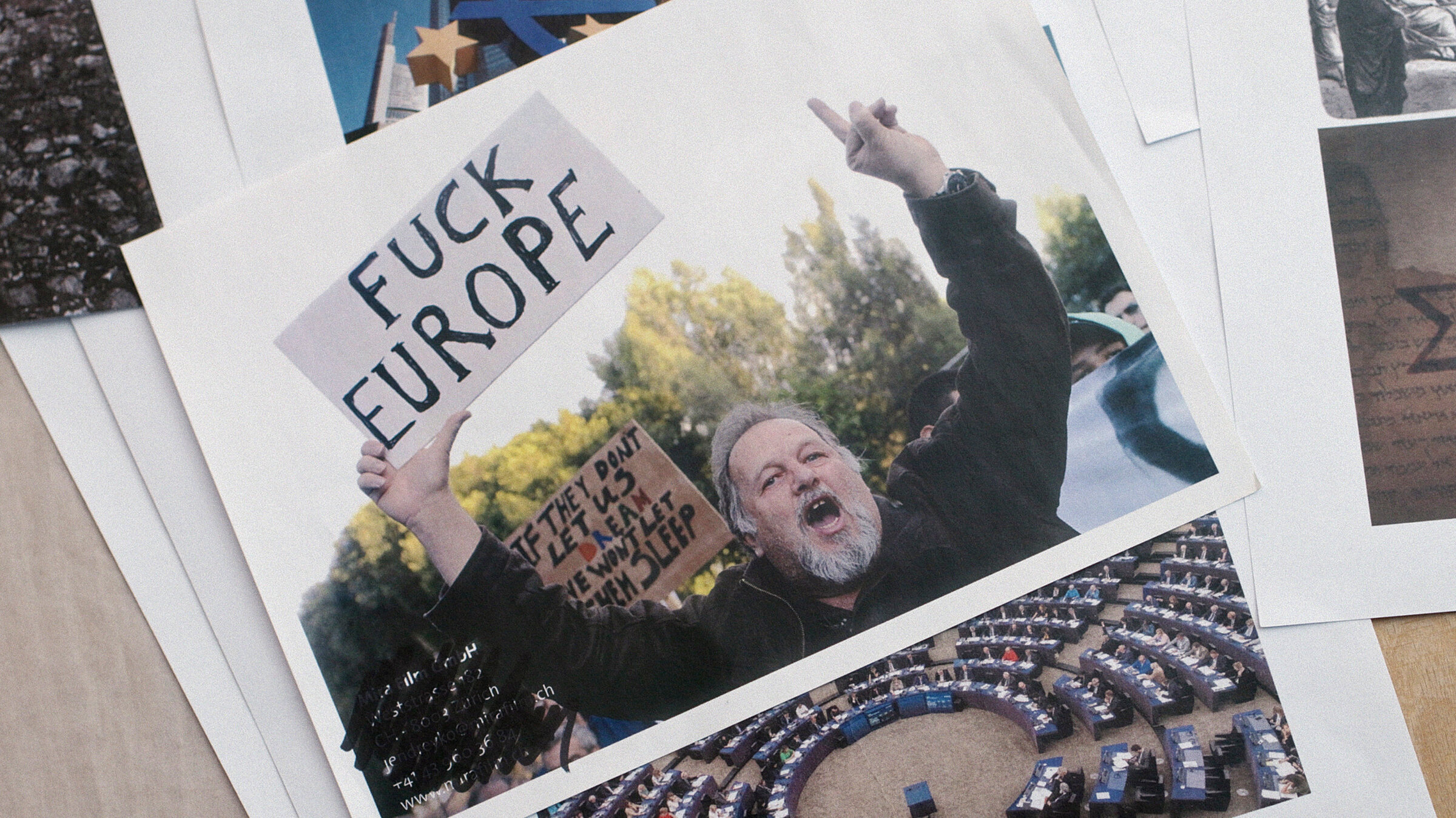 "Das Lied der anderen": Polaroidbilder liegen auf einem Tisch ausgebreitet. Auf einem erkennt man den Plenarsaal des EU-Parlaments, auf einem anderen einen Demonstranten, der ein Plakat hochhält, auf dem „Fuck Europe“ zu lesen ist.