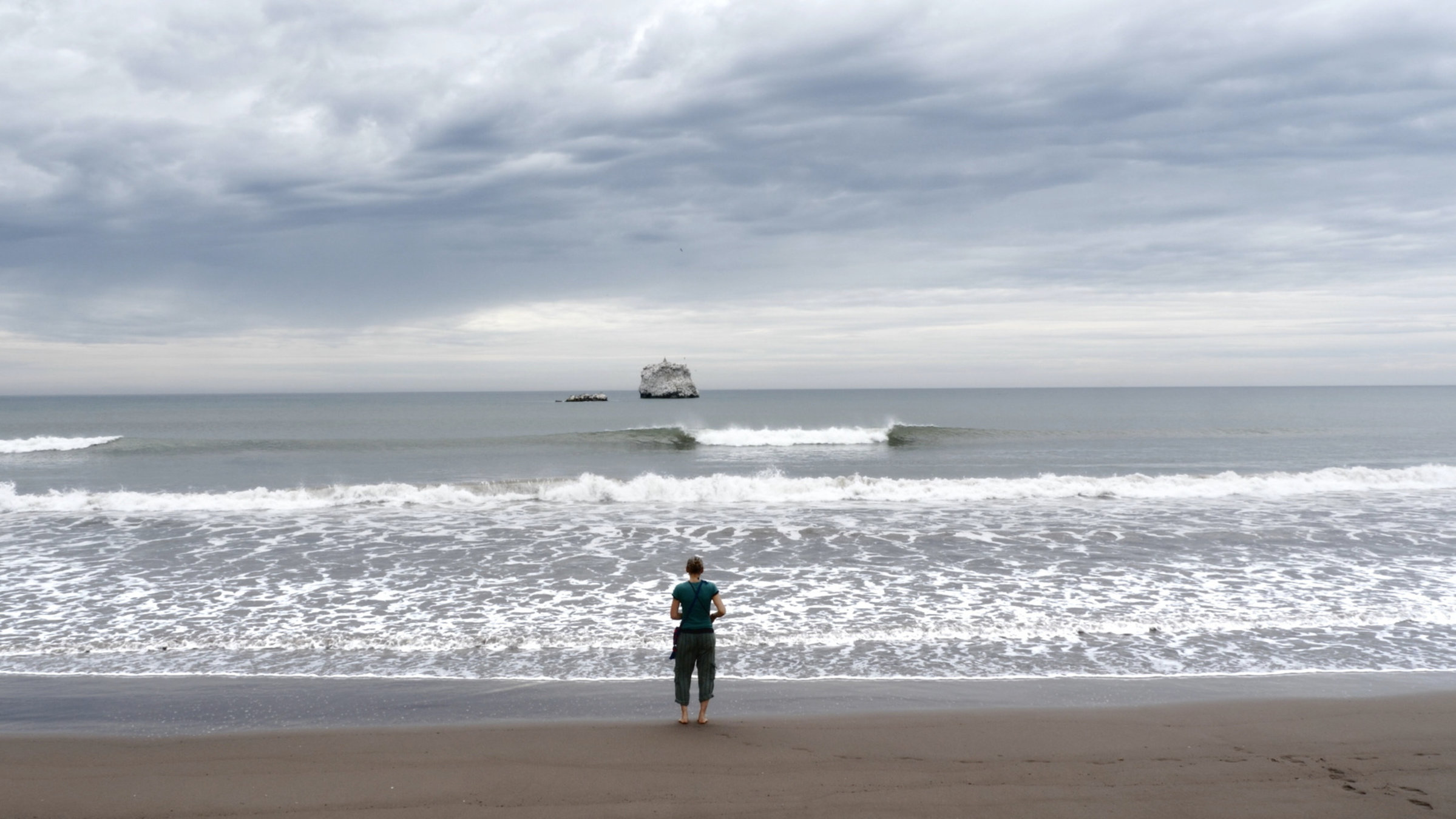 "Aware - Reise in das Bewusstsein": Frau mit dem Rücken zur Kamera am Strand vor Meer.