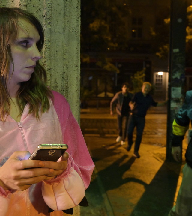 "SOKO Potsdam - Leben lassen": Luna Kunath (Caroline Erikson) steht im rosa Kostüm an einer Straßenecke. Sie hält ein Handy in der Hand und schaut ums Eck, wo ein Mann mit Kappe vorbeirennt.