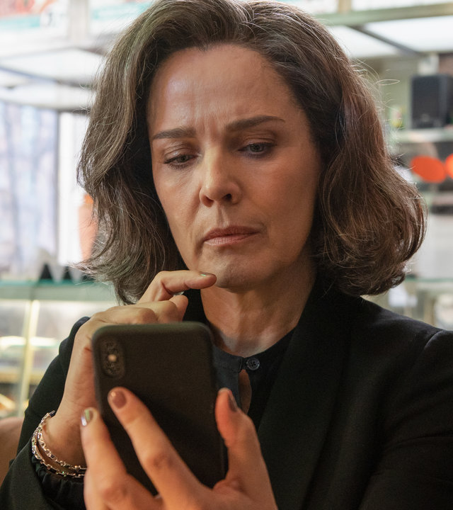 "Bad Banks - Bankensterben": Christelle Leblanc (Désirée Nosbusch) sitzt in einem Café und schaut konzentriert auf ihr Handy. Im Hintergrund steht Thao Hoang (Mai Duong Kieu) und beobachtet sie.