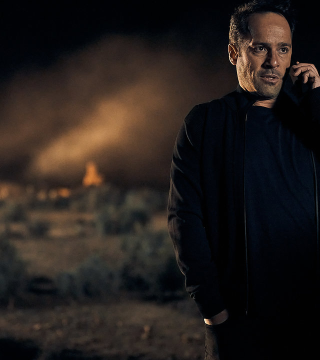 "The Tourist: Precious Memories": Drogenboss Kosta (Alex Dimitriades) steht im nächtlichen Outback neben seinem Auto und telefoniert. Im Hintergrund sieht man die beleuchteten "Steinmänner".