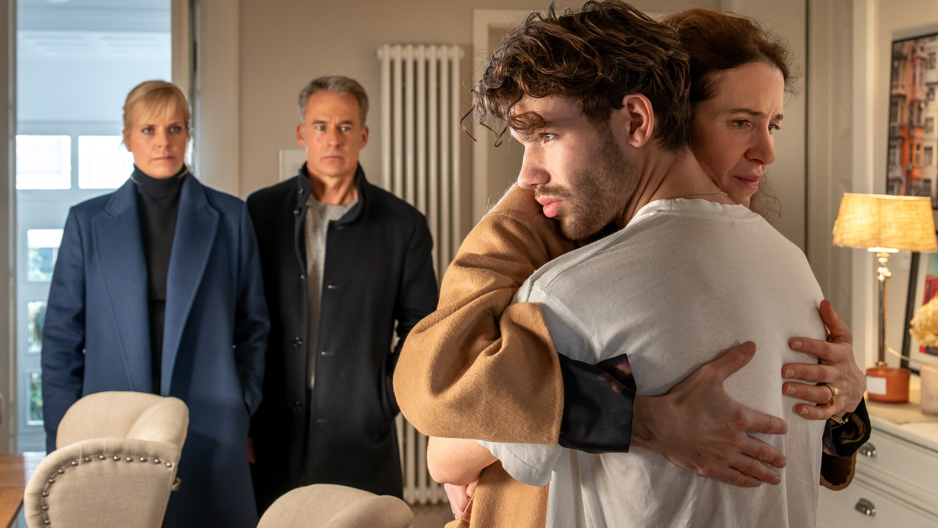 "SOKO Leipzig - Plankton": Ina Zimmermann (Melanie Marschke) und Jan Maybach (Marco Girnth) stehen im Hintergrund eines Zimmers während Noah Gansert (Valentin Oppermann) Rike Gansert (Julia Malik) umarmt. Beide schauen traurig drein.