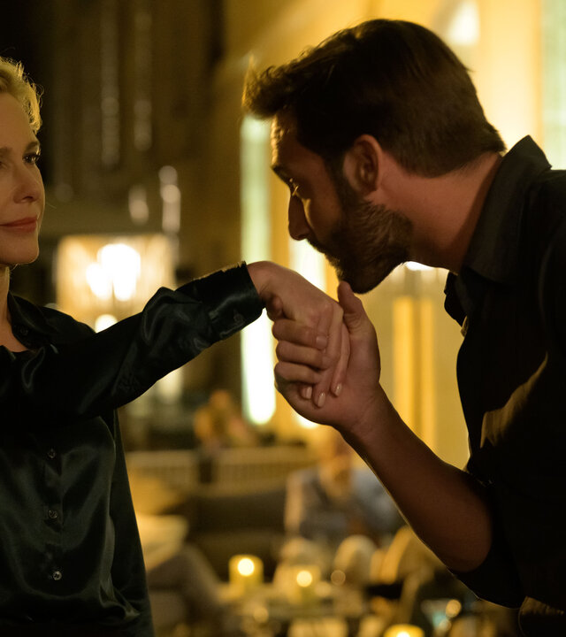 "Escort Boys - Kundenzufriedenheit": Ben (Guillaume Labbé) und Béa (Pascale Arbillot) stehen auf einer Straße. Ben hält Béas Hand und küsst sie, während Béa ihn mit einem leichten Grinsen ansieht. Im Hintergrund stehen Tische, an denen Leute sitzen.