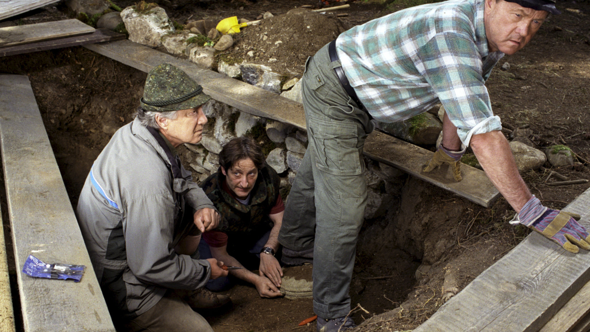 "Forsthaus Falkenau - Schatzsuche": Förster Martin Rombach (Christian Wolff) und Breitkreuz (Hans Stadlbauer) und ein Sprengmeister (Robert Spitz) sind in einem abgesperrten Bereich aus Holz. Breitkreuz steht auf einer Miene und der Sprengmeister hält seinen rechten Fuß fest. Sie wirken besorgt.