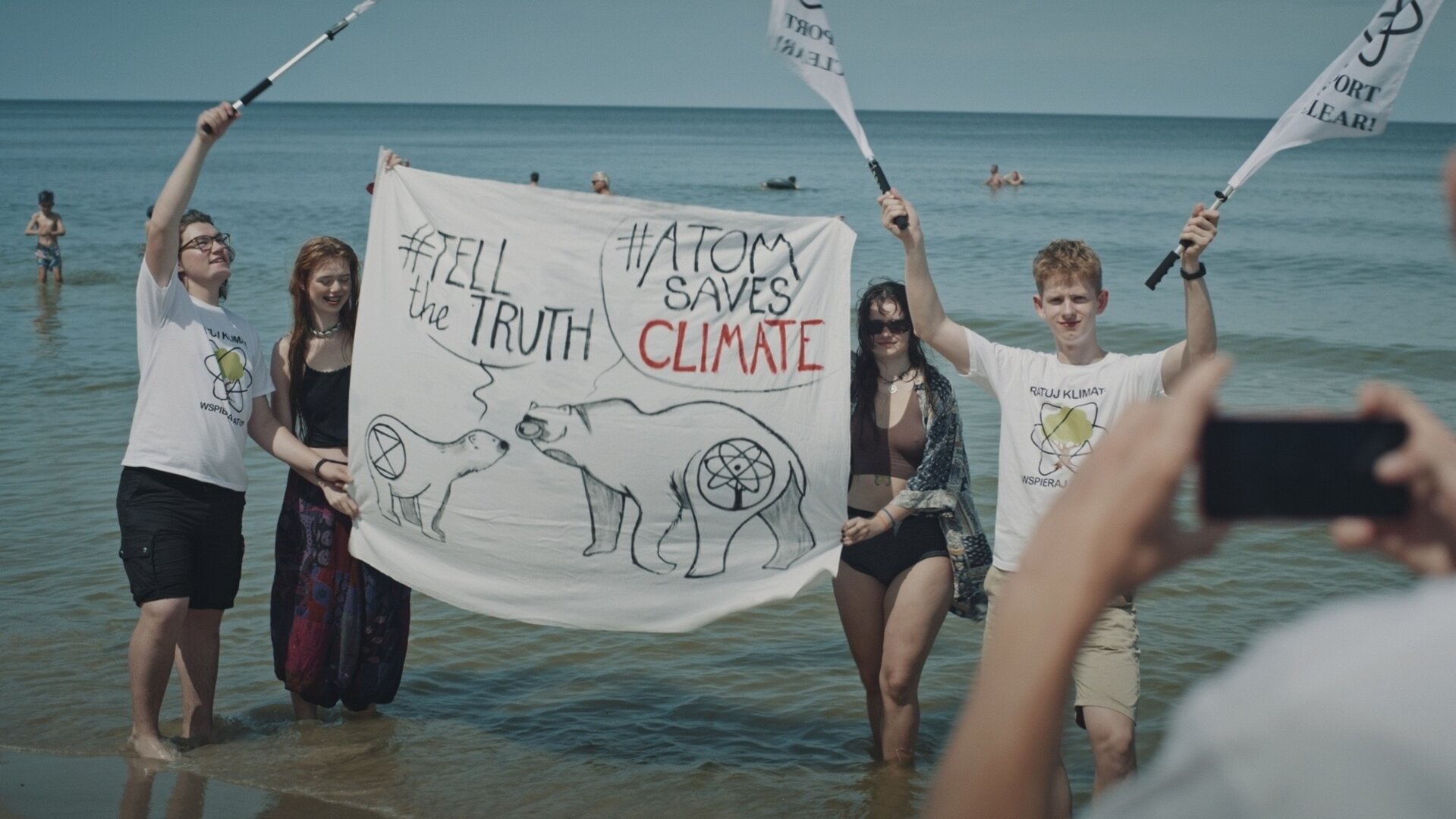 "Spaltung": Jugendliche stehen im Wasser und halten ein Protesttransparent und Fahnen ihrer Organisation für ein Foto in die Kamera.