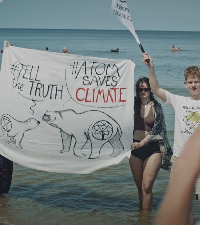 "Spaltung": Jugendliche stehen im Wasser und halten ein Protesttransparent und Fahnen ihrer Organisation für ein Foto in die Kamera.