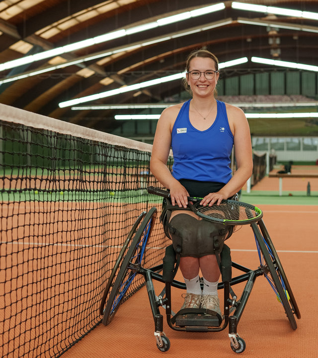 "einfach Mensch: Britta Wend - Tennis für Alle!": Britta Wend sitzt in ihrem Sportrollstuhl auf dem Tennisplatz. In der Hand hält sie ihren Tennisschläger.