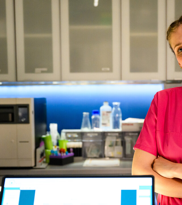 "Bettys Diagnose - Stunde der Wahrheit": Frida (Johanna Hens) steht mit verschränkten Armen Ivo (Oscar Nadermann) gegenüber, der vor einem Laptop sitzt, und schaut ihn an. Im Hintergrund hängt ein Arzneischrank an der Wand und darunter stehen verschiedene Behandlungsutensilien.