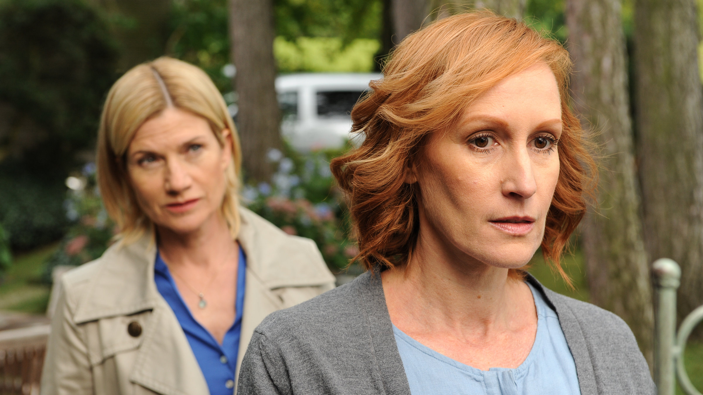"SOKO Stuttgart - Seitenwechsel": Martina Seiffert (Astrid M. Fünderich) steht hinter Marlene Hahn (Nicole Beutler) und beobachtet sie genau. Sie befinden sich im Garten. Im Hintergrund ist unscharf ein weißer Lieferwagen zu sehen.