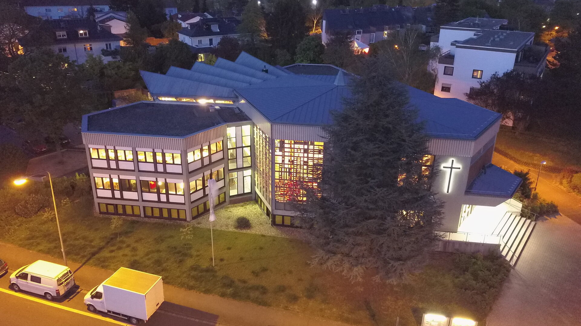 "Evangelischer Gottesdienst - Trau dich, zu vertrauen": Auf dem Bild ist die 1974 eingeweihte Christuskirche in Wiesbaden, auch Kirche überm Wellritztal genannt, von oben zu sehen. Es ist Abend, durch die vielen Fenster scheint das Licht aus dem sechseckigen Gottesdienstsaal und aus den Fenstern des angebauten Gemeindezentrums der deutschen Baptistengemeinde und der englischsprachigen International Baptist Church.