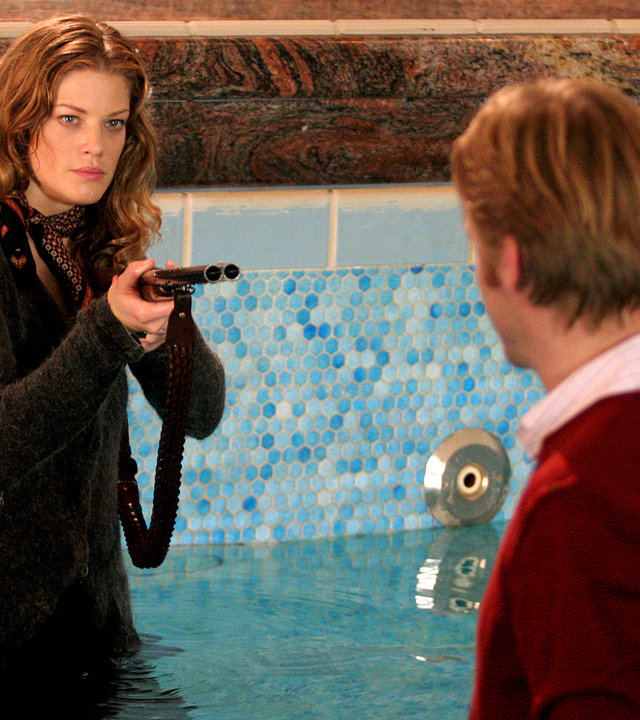 "Der letzte Zeuge - Im gläsernen Sarg": Emma Berg (Marie Bäumer) bedroht ihren Chef Hans Forbach (Kai Scheve) mit einem Gewehr. Sie stehen bis zur Hüfte in einem Pool.