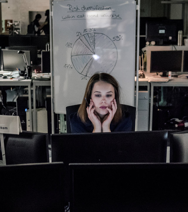 "Bad Banks - Die Kündigung": Jana Liekam (Paula Beer) sitzt an ihrem Schreibtisch hinter mehreren Bildschirmen und arbeitet. Es scheint spät zu sein, denn die anderen Arbeitsplätze im Großraumbüro sind leer.