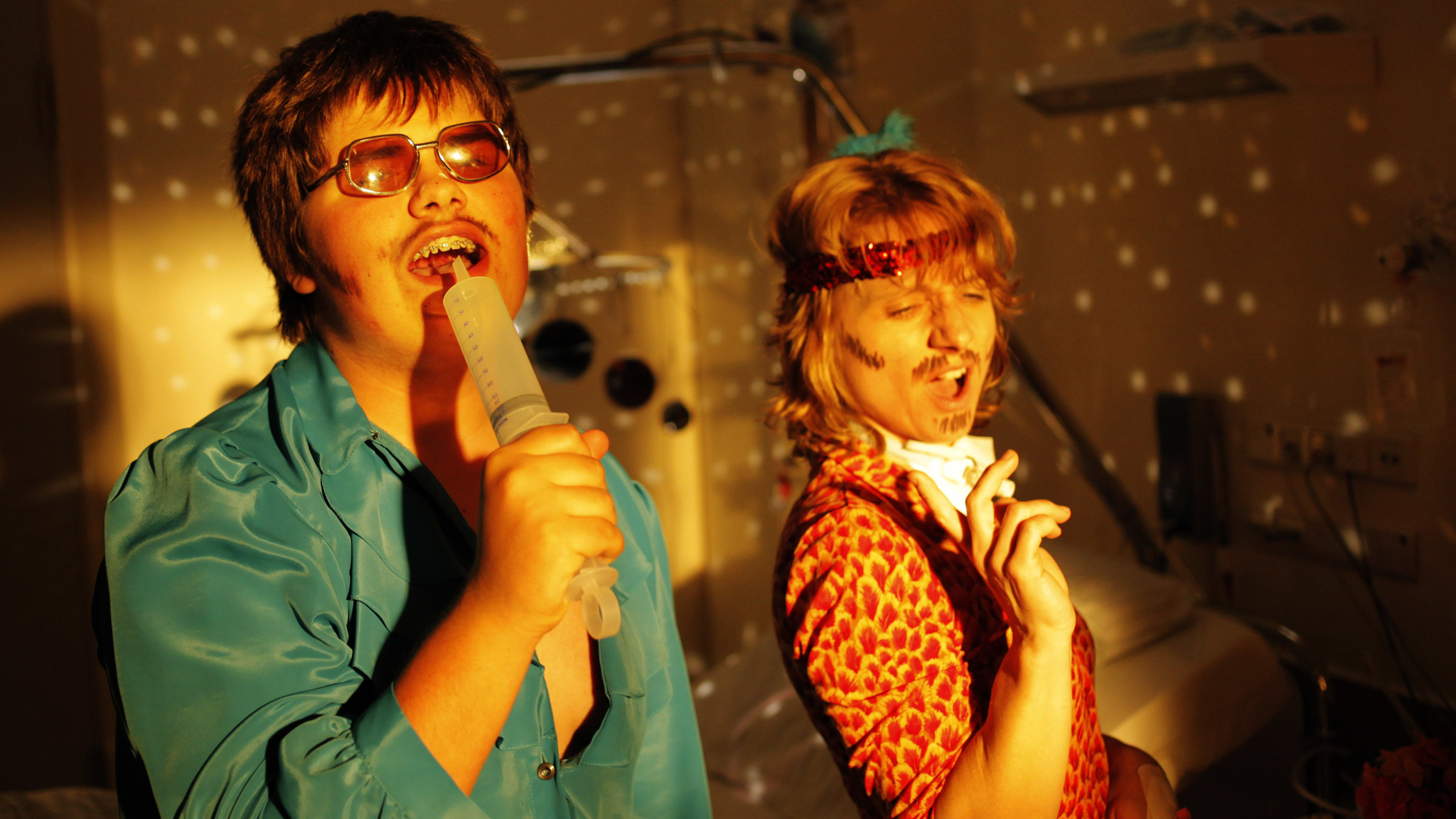 "Ich fühl mich Disco": Florian Herbst (Frithjof Gawenda) und seine Mutter Monika (Christina Große) haben sich verkleidet und singen gemeinsam. Florian nutzt eine leere Spritze als Mikrofon.