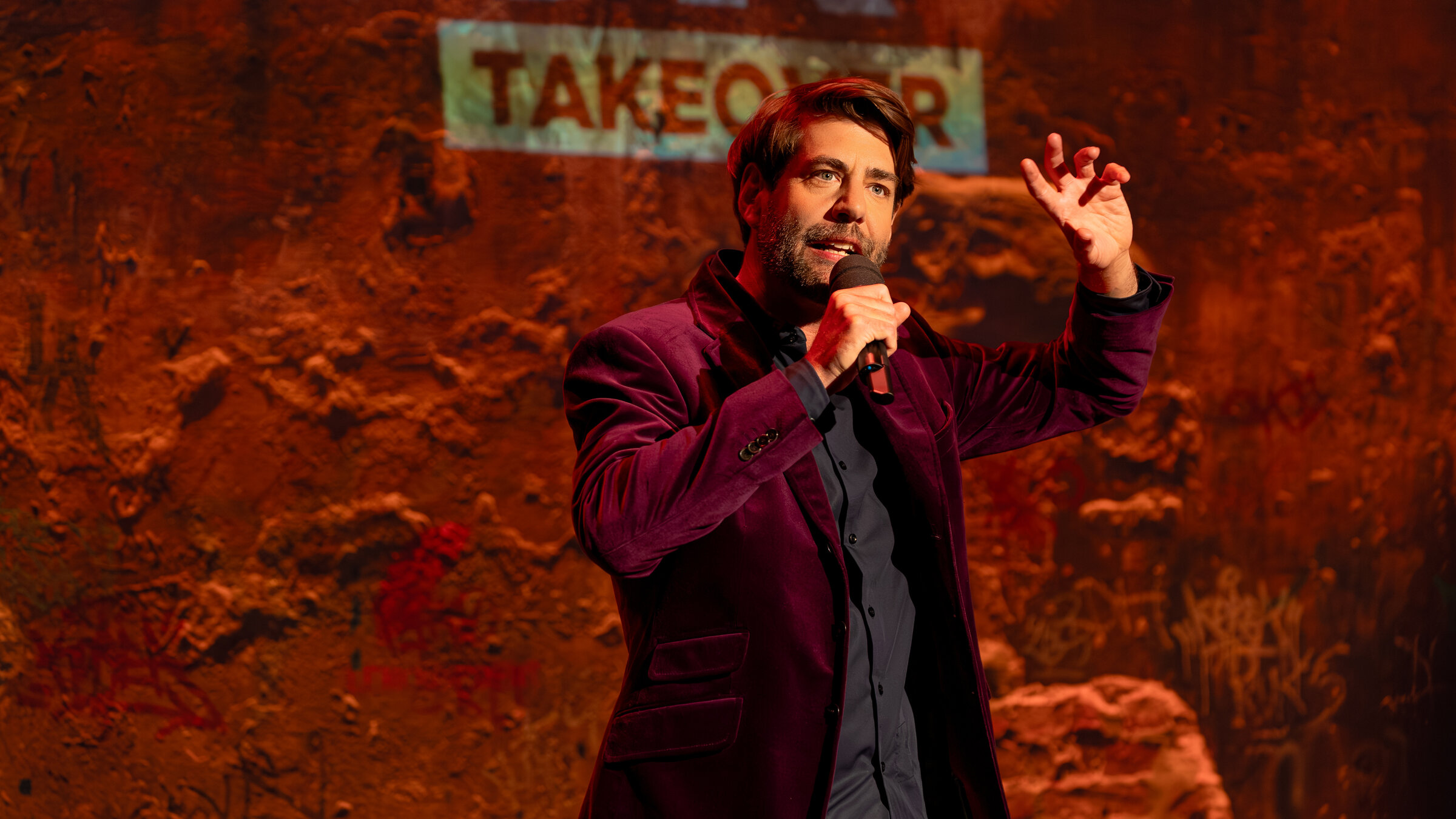 "Till Reiners` Happy Hour - Takeover - Primetime-Comedy mit Claus von Wagner und Gästen": Der Kabarettist und Gastmoderator Claus von Wagner steht mit einem Mikrofon in der Hand auf der Bühne und gestikuliert