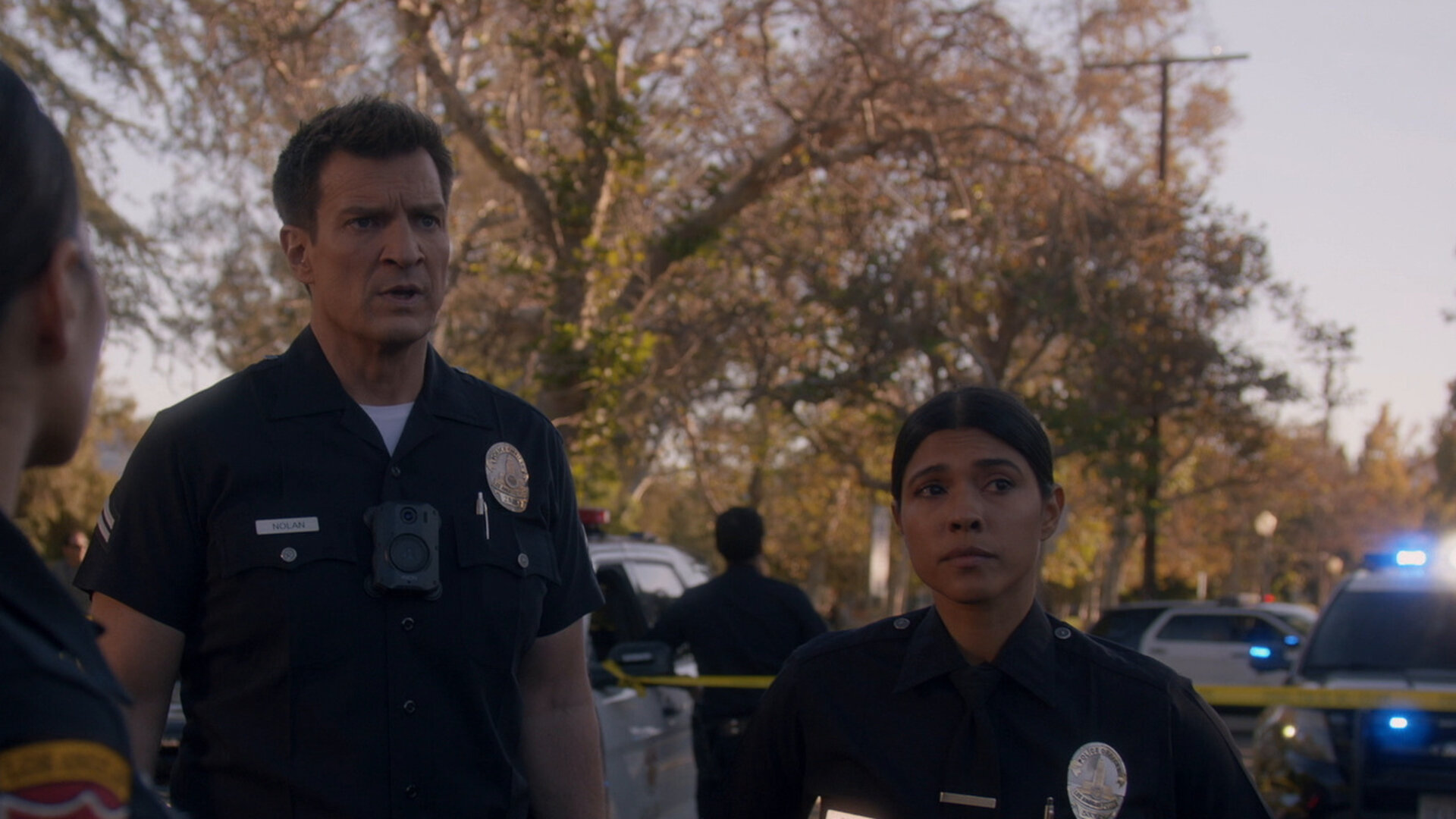 "The Rookie - Todesurteil": Officer John Nolan (Nathan Fillion) und Officer Celina Juarez (Lisseth Chavez) stehen auf einer abgesperrten Straße, umgeben von Polizeifahrzeugen. Ihre Blicke sind ernst und richten sich in die gleiche Richtung.