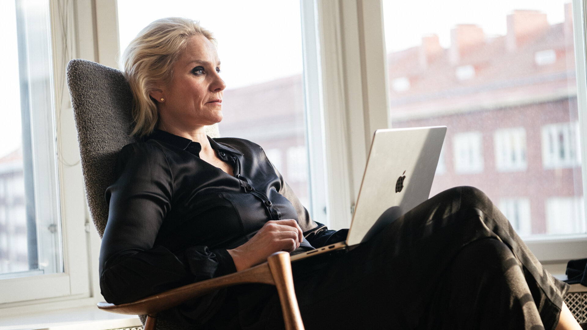 "Queen of Fucking Everything - Zahltag": Linda (Laura Malmivaara) sitzt in einem Raum vor einer Fensterfront. Auf ihrem Schoß steht ein aufgeklappter Laptop.