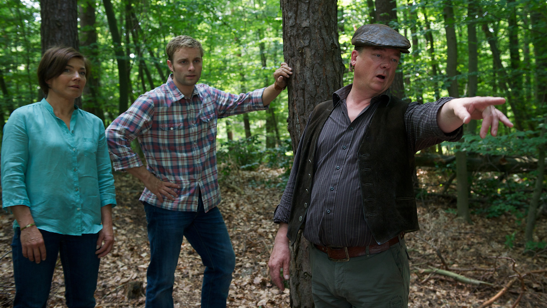 "SOKO Wismar - Fotofalle": Katrin Börensen (Claudia Schmutzler) und Nils Theede (Jonas Laux) stehen im Wald mit dem Jagdpächter Hansjörg Strack (Peter Kurth), der mir einer Hand auf etwas weiter vorne zeigt.