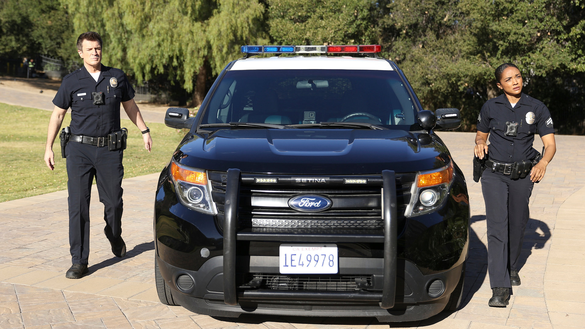 "The Rookie - Ein gefallener Stern": Nolan (Nathan Fillion) und Harper (Mekia Cox) laufen neben einem Streifenwagen her, der in einer Einfahrt geparkt ist.