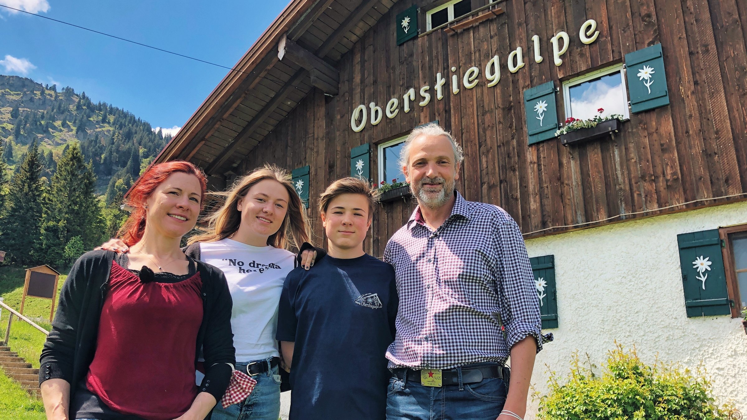 "Terra Xpress: Neustart auf der Alm und Gefahr unterm Gipfelkreuz": Eine Familie, Vater, Mutter, Sohn und Tochter stehen vor einem alten Bauernhaus auf einer Wiese. Darauf steht "Oberstiegalpe".