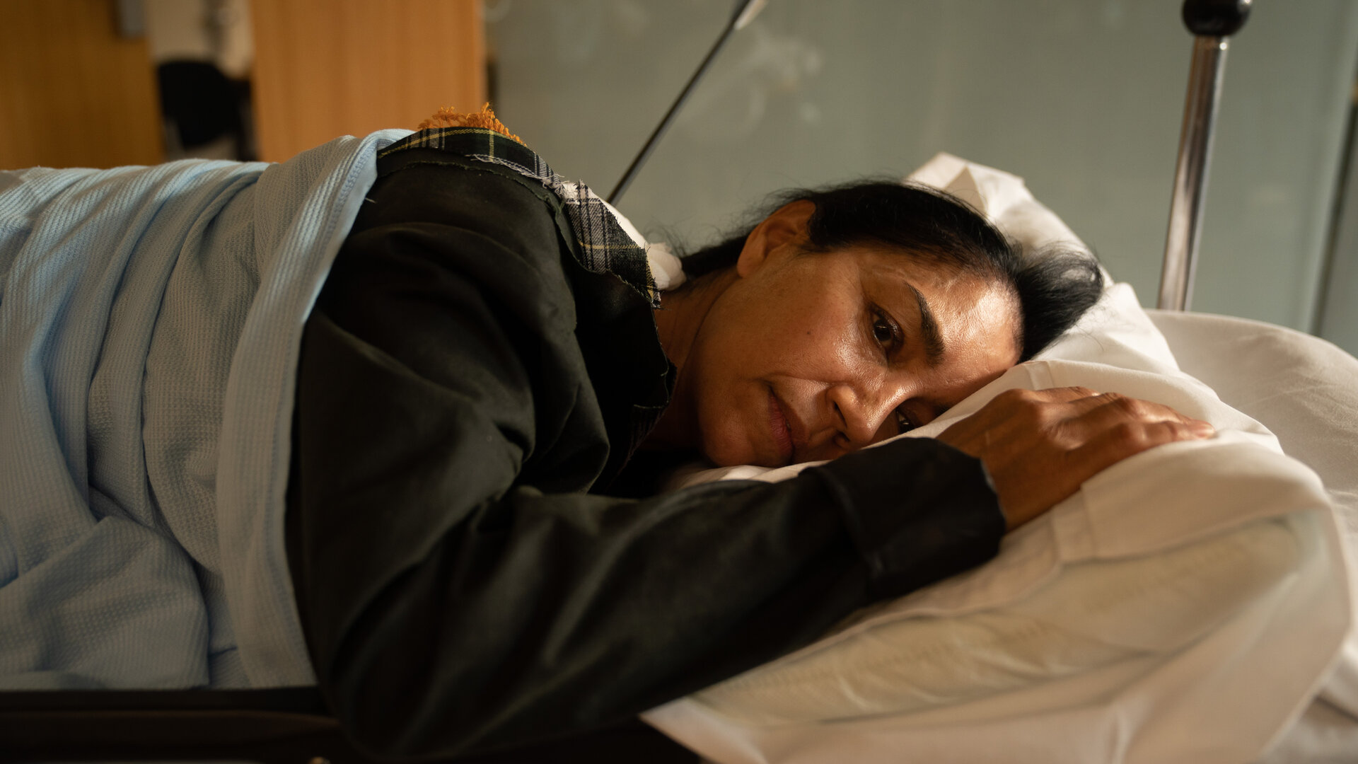 "Beyond Paradise - Getroffen": Niamh Kirby (Seeta Indrani) liegt mit erschöpftem Gesichtsausdruck in einem Krankenbett auf der Seite. Aus ihrem Rücken ragt ein Pfeil.