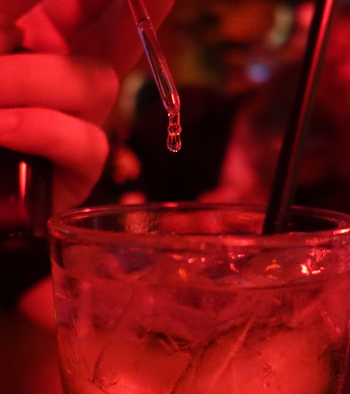 "37°: K.o. getropft - Leben nach dem Filmriss": Spielszene in einer Bar: Die rote Beleuchtung taucht die Bar in eine mystisch-schummrige Stimmung. Jemand träufelt mit einer Pipette Tropfen in ein gefülltes Glas.