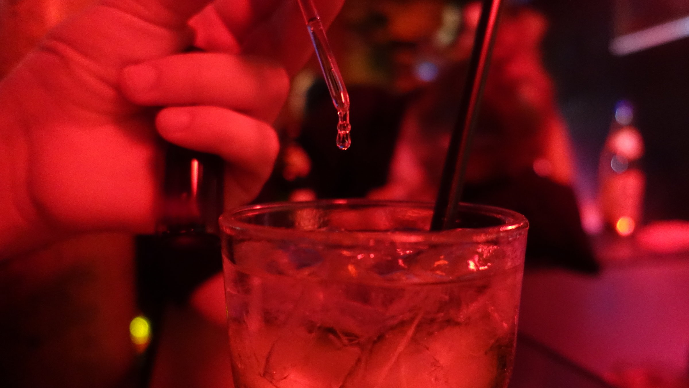 "37°: K.o. getropft - Leben nach dem Filmriss": Spielszene in einer Bar: Die rote Beleuchtung taucht die Bar in eine mystisch-schummrige Stimmung. Jemand träufelt mit einer Pipette Tropfen in ein gefülltes Glas.