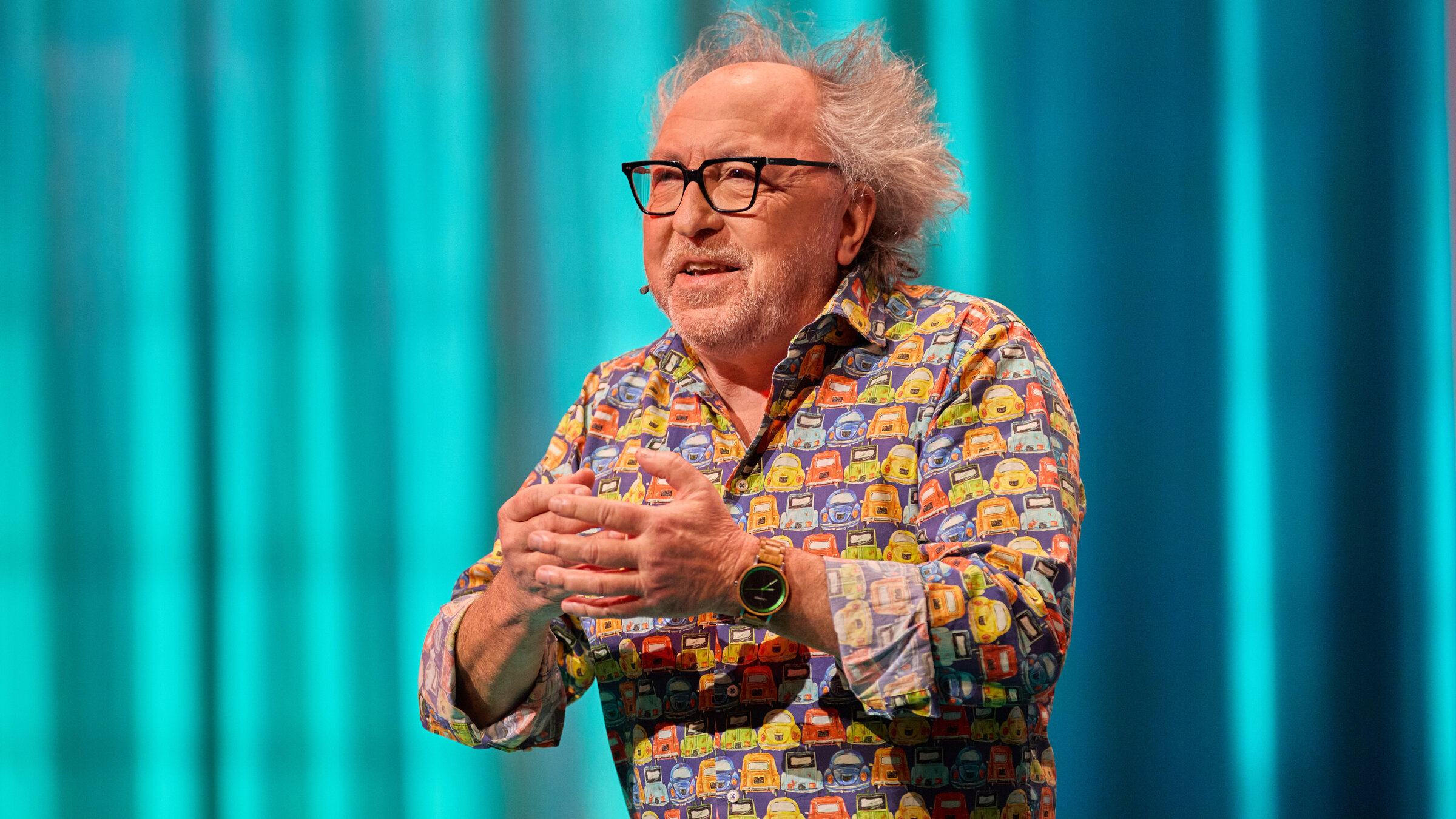 "TILT!": Urban Priol ist in der Mitte des Bildes zu sehen. Er hält die Hände vor seiner Brust. Sein Hemd ist bunt. Er trägt eine Brille.