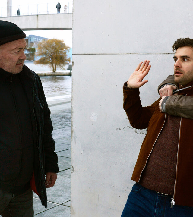 "Ein starkes Team - Fast perfekte Morde": Im Freien am Flussufer: Otto Garber (Florian Martens) blickt auf eine bedrohliche Situation und hält seine Hand an seine Dienstwaffe am Gürtel. Vor ihm hält Dennis Zander (Björn von der Wellen) den Ermittler Nils Makowski (Lucas Reiber) fest und hält ihm eine Messer an die Kehle.