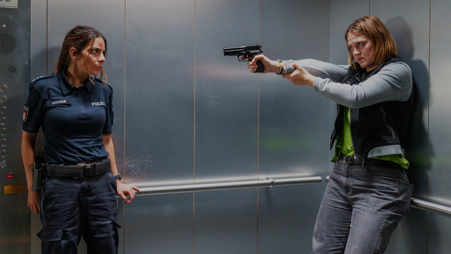 "Notruf Hafenkante - Abwärts": Die Polizistin Isa Nowak (Lilli Hollunder) und Hanna Kampe (Nele Trebs) stehen in einem Aufzug. Hanna hat eine Waffe auf Isa gerichtet. Isa ist an der Stirn verletzt.
