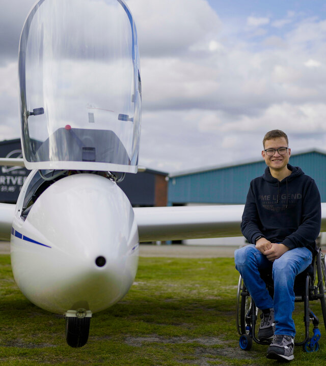 "einfach Mensch - Der Traum vom Fliegen: Jonathan Teupen (1)": Jonathan Teupen sitzt im Rollstuhl neben einem Segelflugzeug.