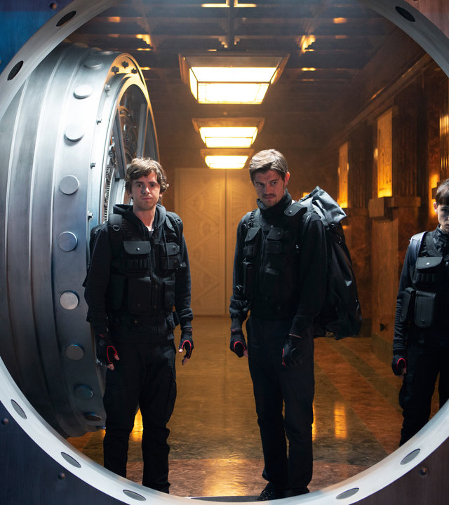 "Countdown in Madrid": Halbtotale. Thom (Freddie Highmore), James (Sam Riley) und Lorraine (Àstrid Bergès-Frisbey) stehen mit angespannten Blicken in offener Tür von Tresorraum. Die Kamera blickt aus dem Tresorraum heraus auf das Trio.