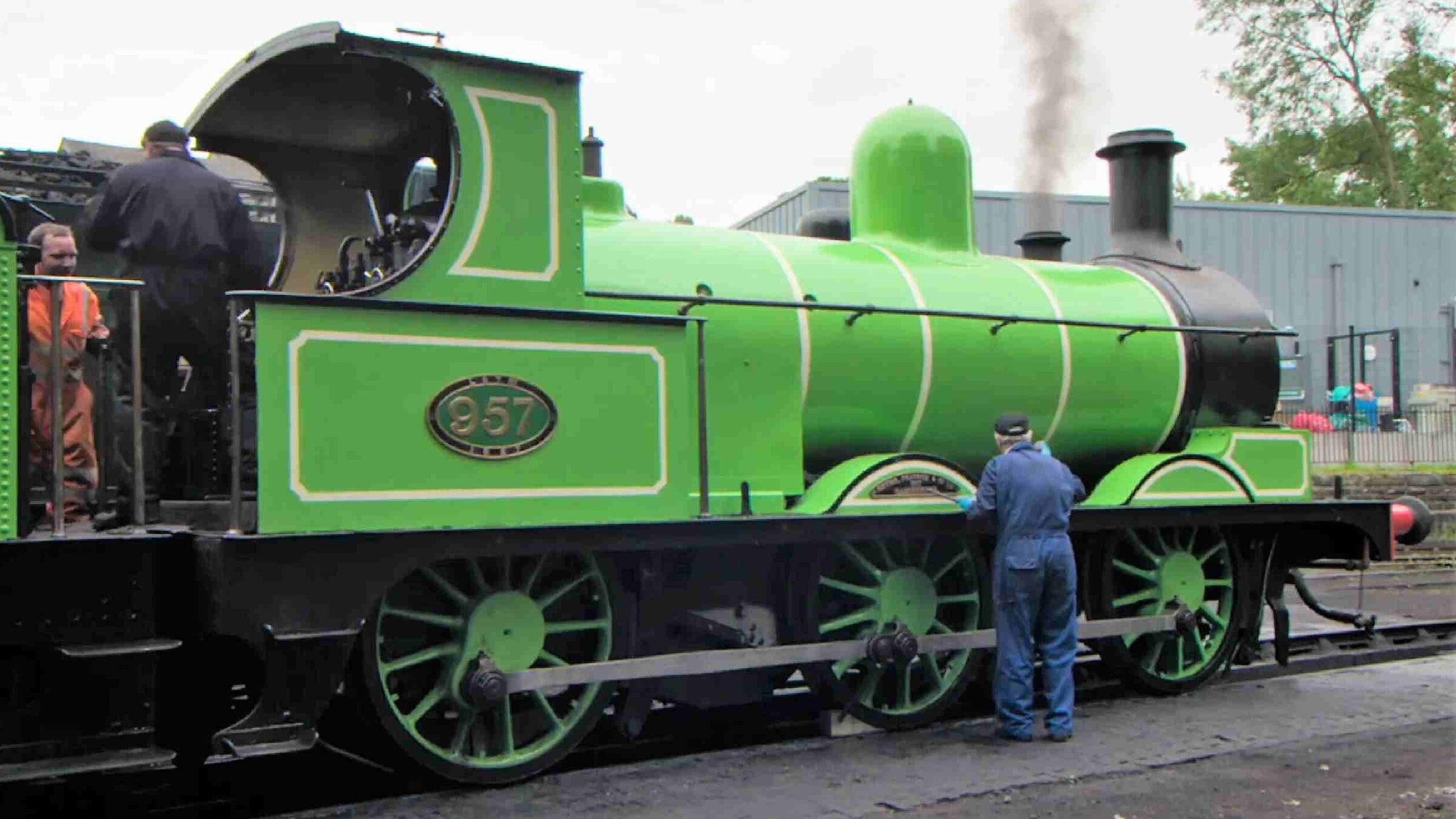 „Großbritanniens schönste Bahnstrecken - Die Rückkehr des Grünen Drachen": Drei Männer in Overalls arbeiten auf einem Bahnsteig an einer grünen Dampflokomotive.