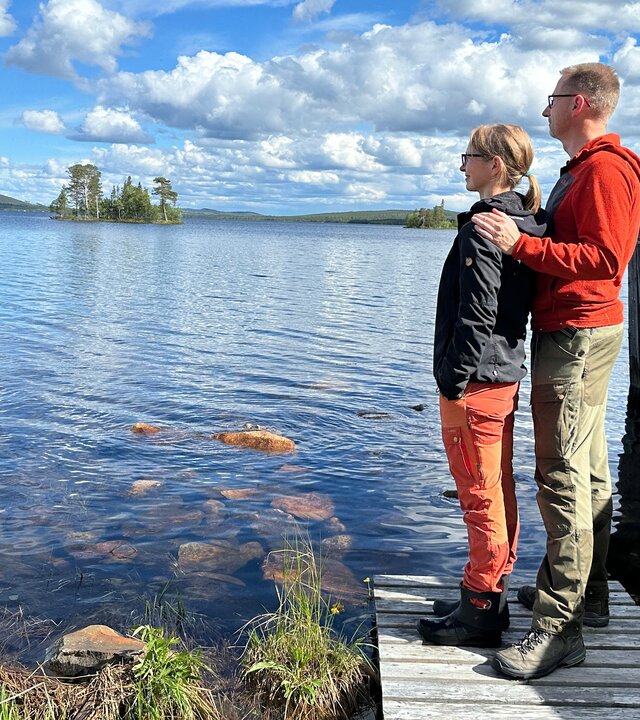 "Abenteuer Auswandern - Neuanfang in Schweden": Andrea Windolph und Alexander Blumenau stehen auf einem Steg am Wasser und schauen seitlich in die Ferne. Die Sonne scheint, am Himmel ziehen Wolken vorbei.