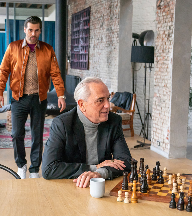 "The Bank Hacker": Alidor Van Praet (Gene Bervoets) spielt Schach mit Bart (Koen De Graeve) an einem Tisch, während Prince (Manuel Broekman) durch den Raum zu ihnen läuft. Im Hintergrund sitzen Ada (Ella-June Henrard) und Souleymane (Claude Musungayi) auf dem Sofa.